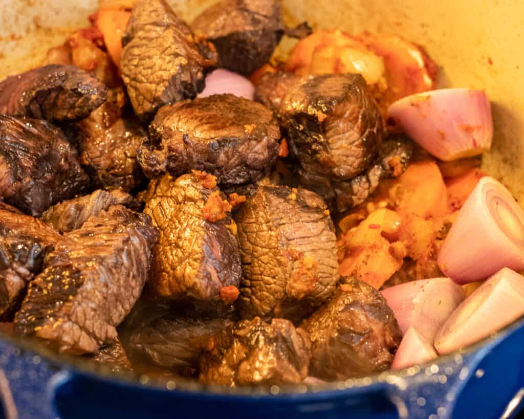 The seared beef and the button onions are added to the pan.