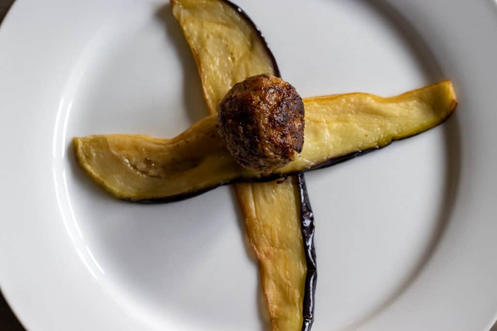 A meatball placed in the middle of two crossed eggplant strips.