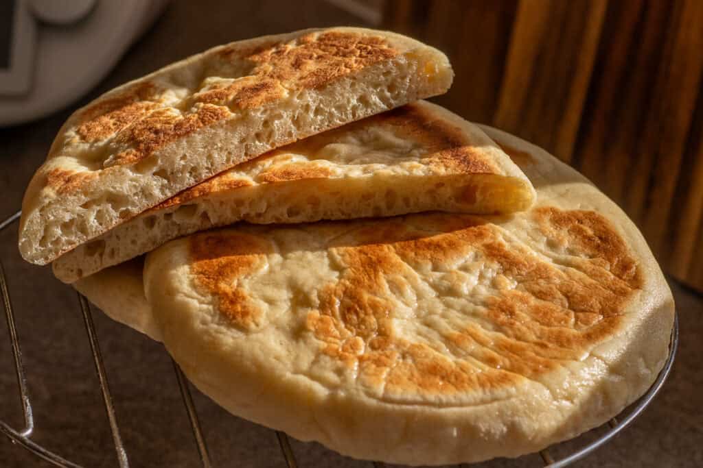 Bazlama bread is cut in half and placed on a wire rack.