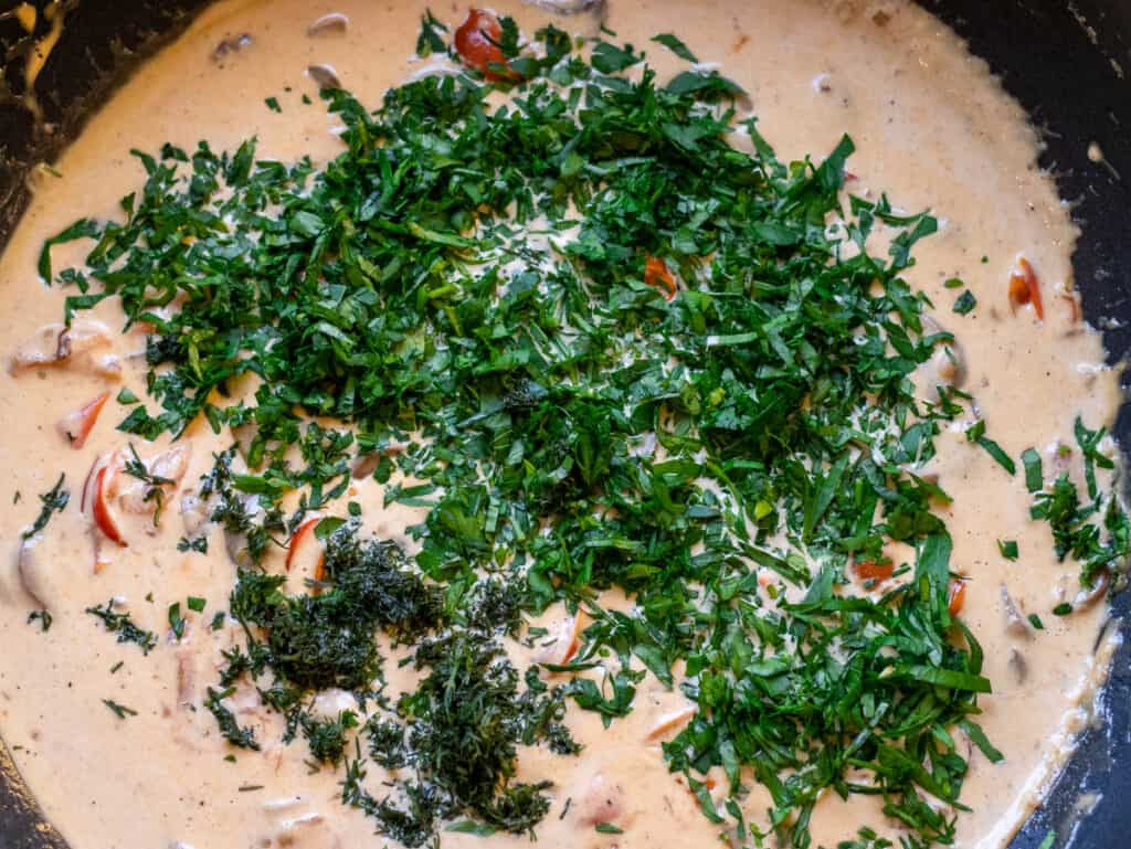 Chopped parsley and dill added to the creamy sauce in the wok.