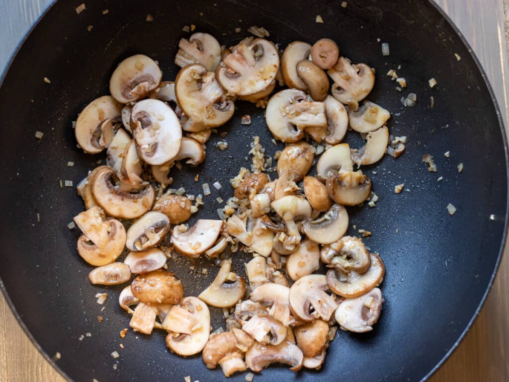 Sliced mushrooms and shallots cooking in a wok.