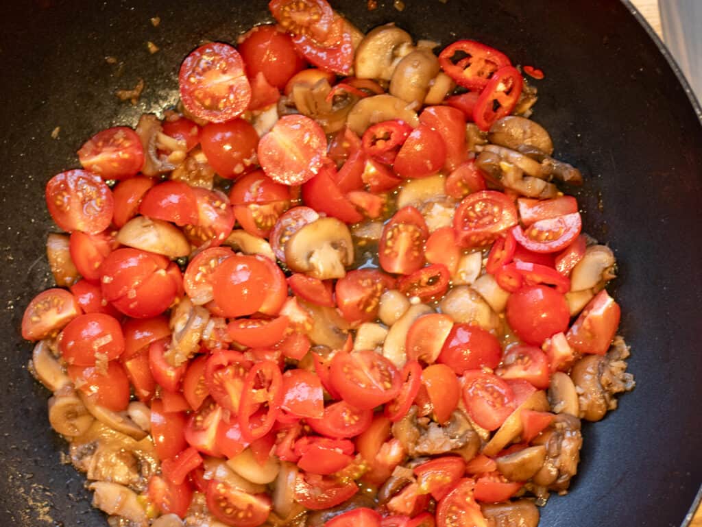 Halved cherry tomatoes added to the mushrooms in the wok.