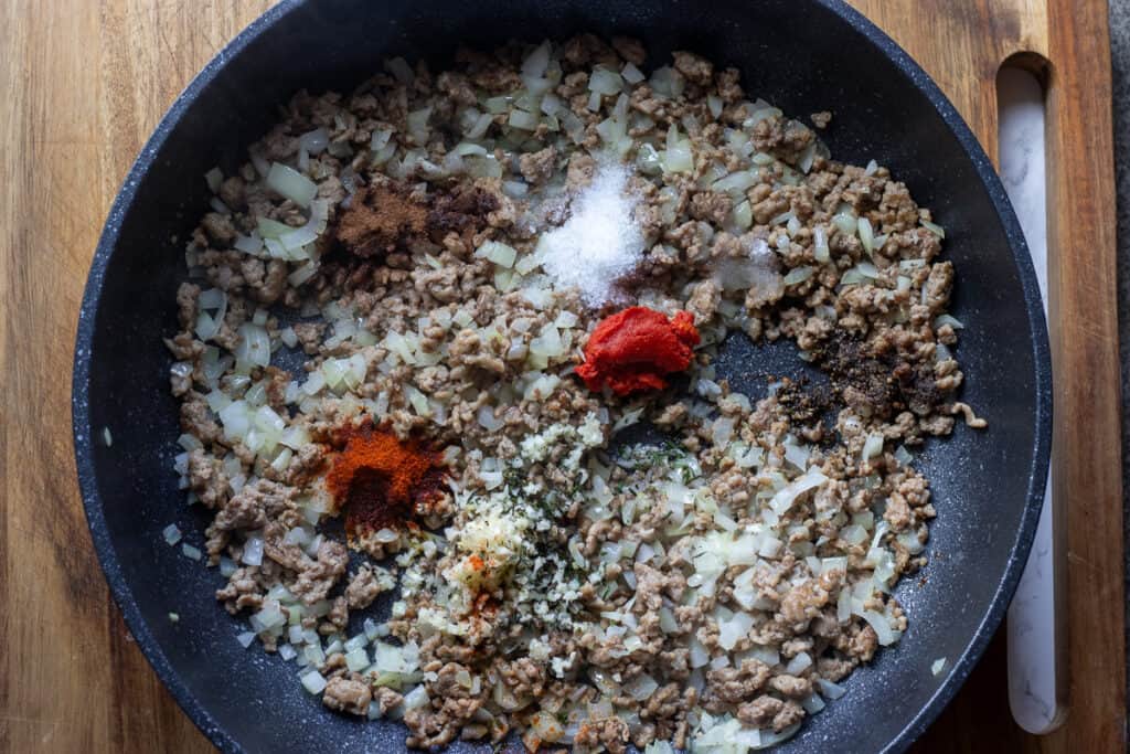 The spices and tomato paste are added to sauteed onions and browned meat.