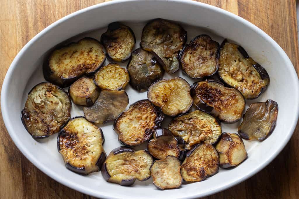 Half of the eggplants are layered to a bottom of a baking dish.