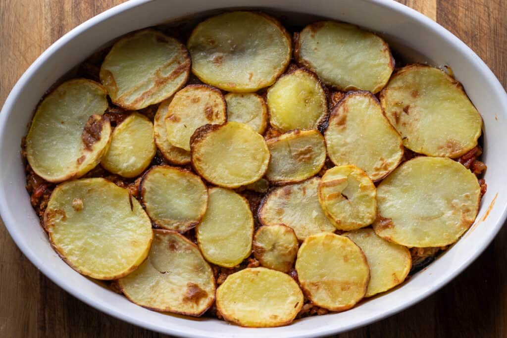 Sliced potatoes are layered on top of the meat filling.