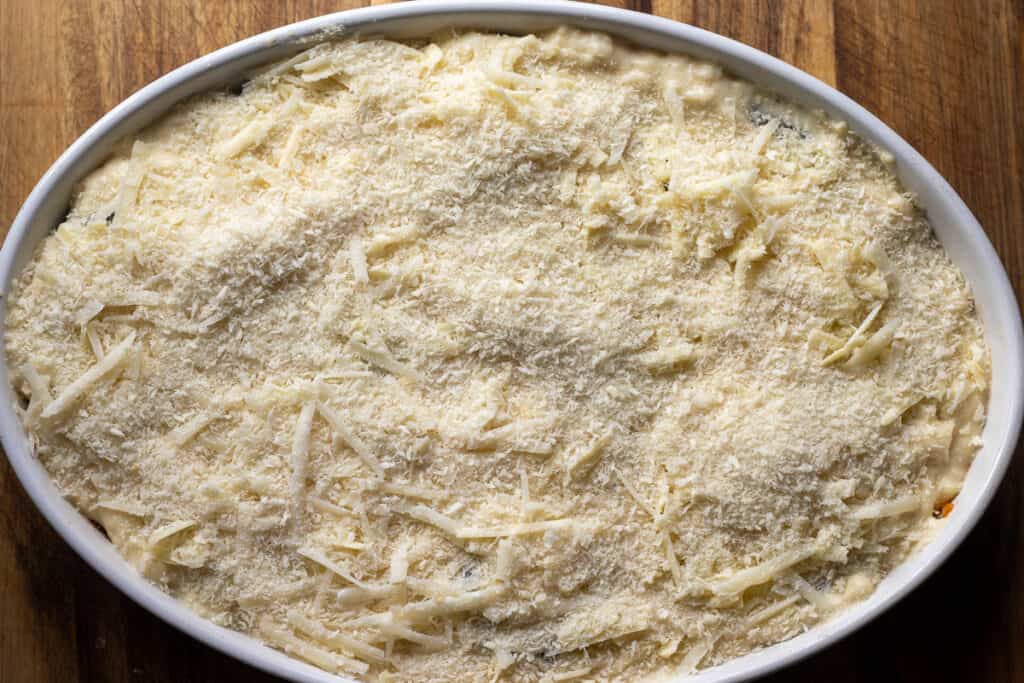 Moussaka is topped with cheese and breadcrumbs before baking.