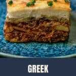 Greek moussaka on a blue plate, cut to show layers of potato, lamb sauce, eggplant and bechamel.