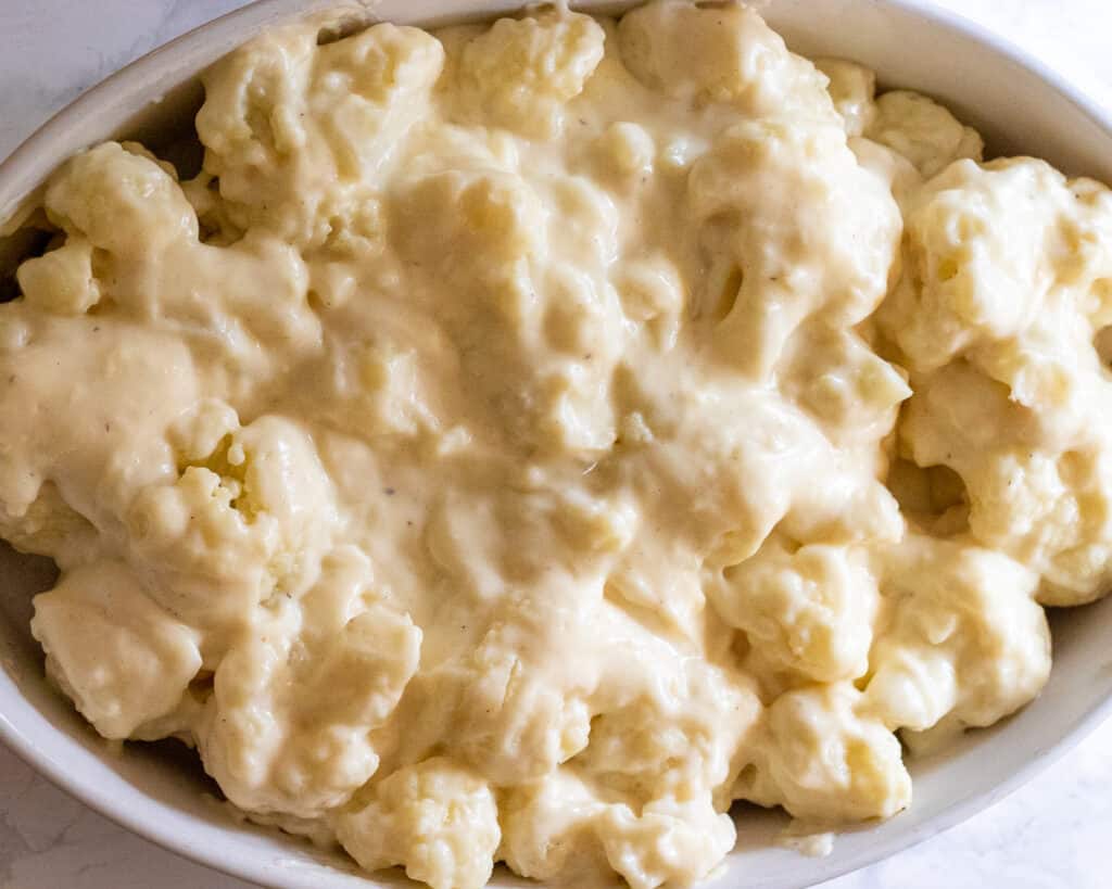 Cauliflower florets covered with the cheese sauce in a baking dish.