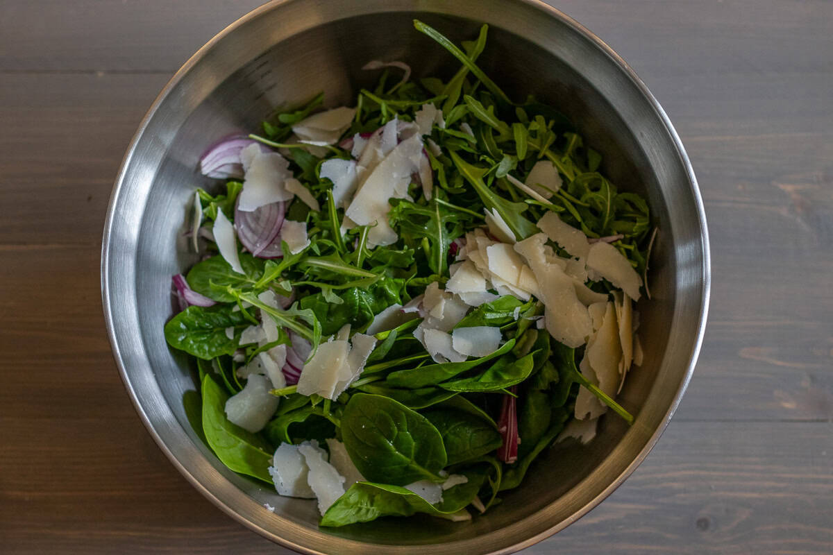 frsh leaves are placed in a bowl and topped with sliced red onions and parmesan shavings.