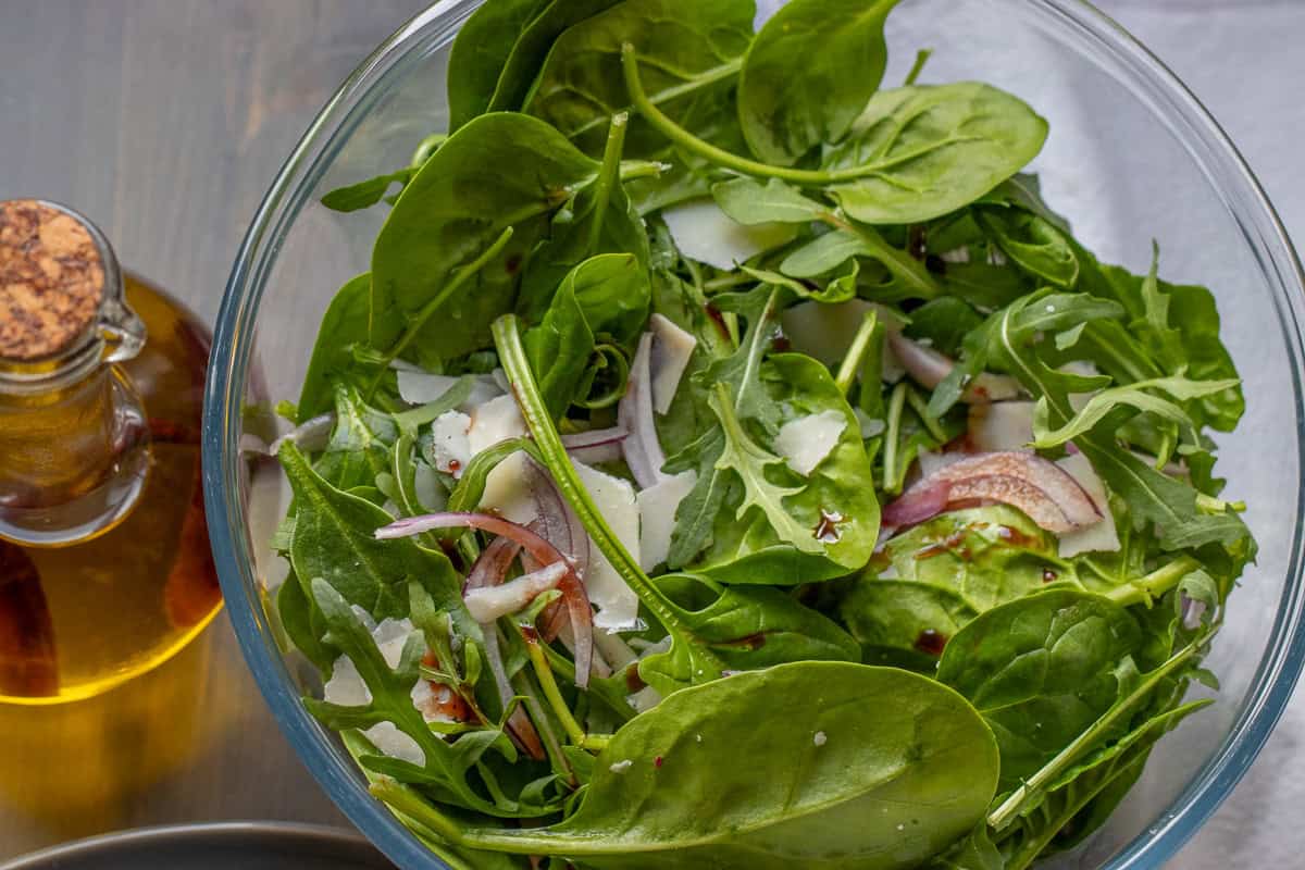 Green salad in a glass bowl with a bottle of olive oil on the side.