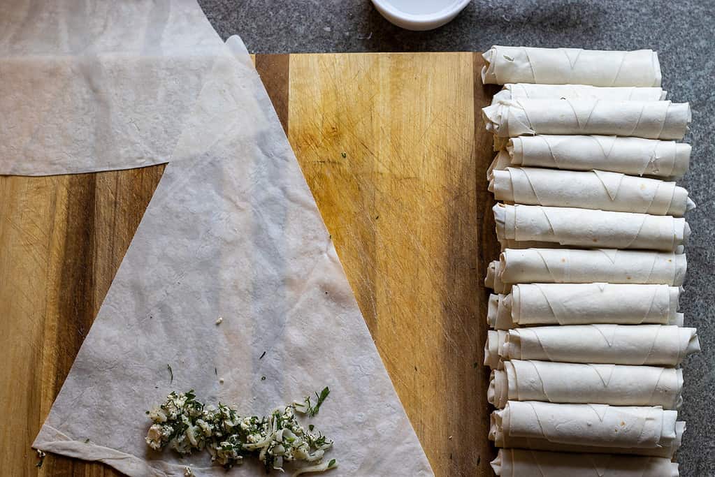 Rolled boreks lined up in rows next to a filled yufka triangle.