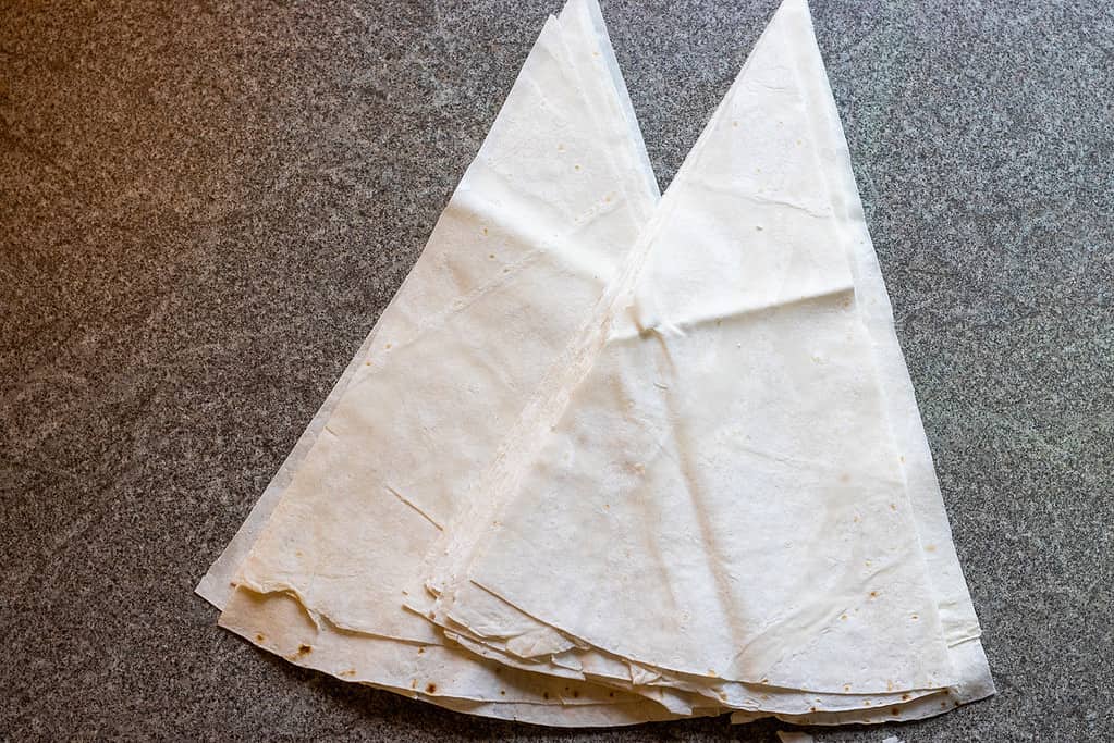 Yufka sheets cut into large triangles and stacked on a work surface.