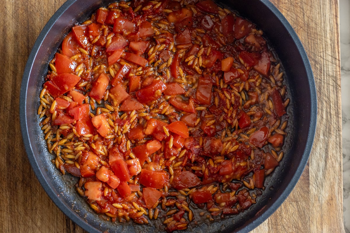 The chopped tomatoes, tomato paste, and sun-dried tomatoes are added to browned orzo.