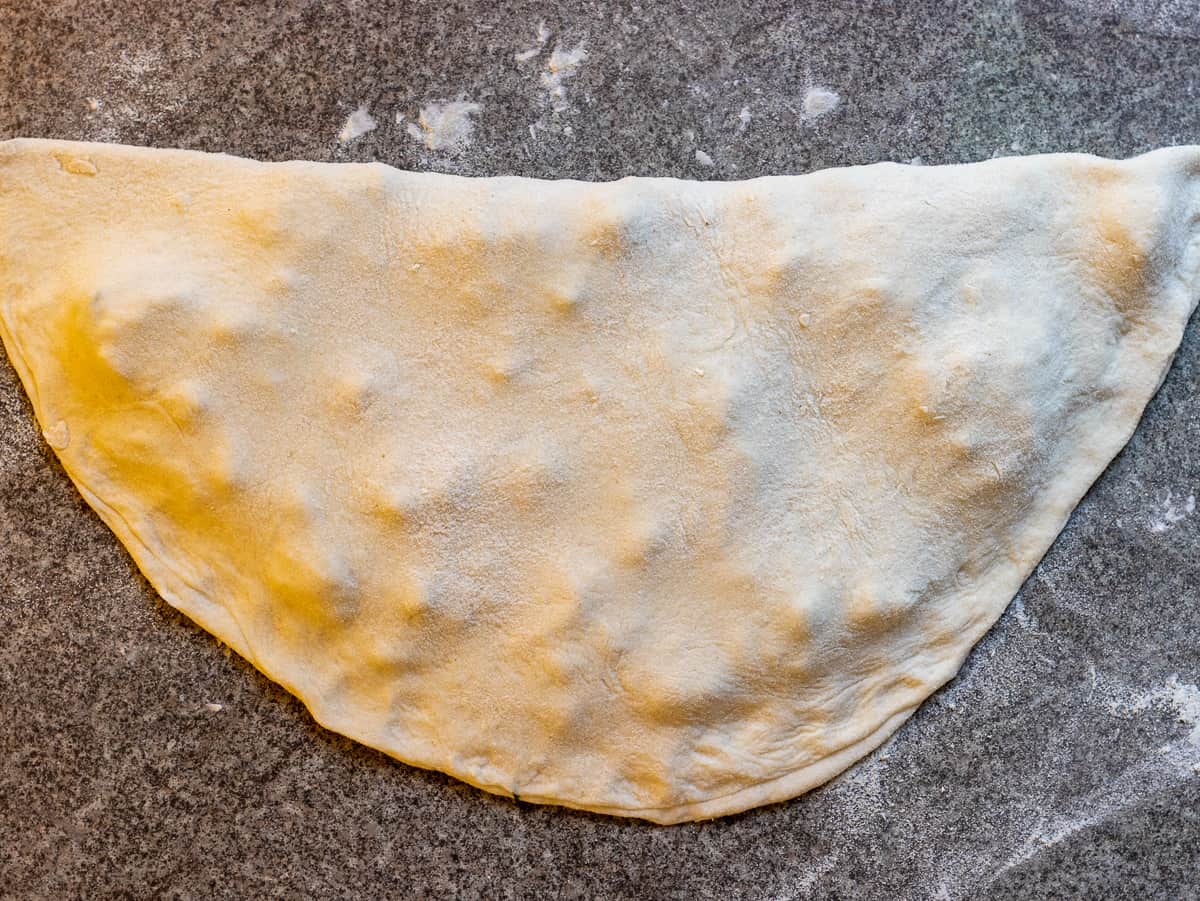 The other half of the dough is folded over the filling and the seams of the gozleme are pinched to shut.