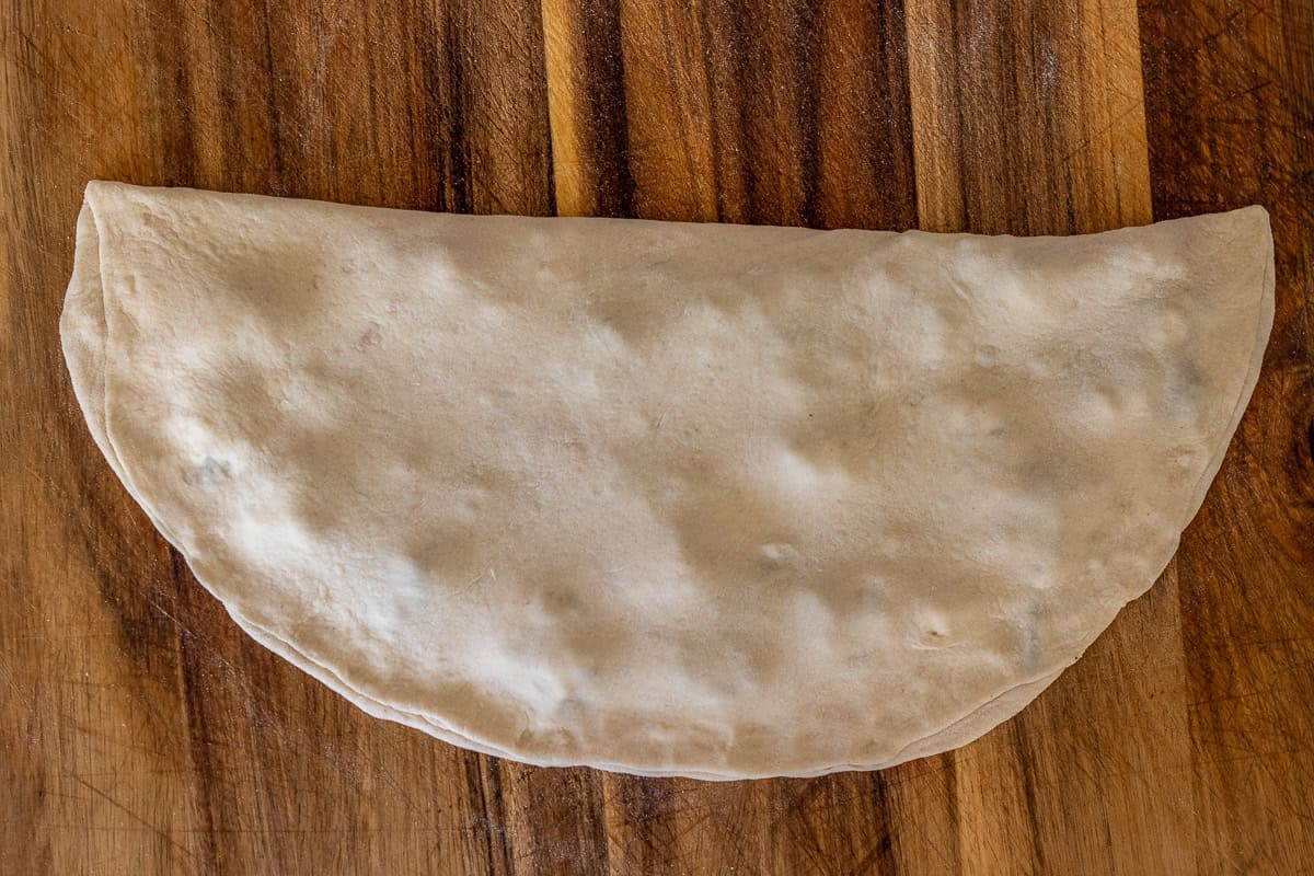 The other half of the dough is folded over the filling and the seams of the gozleme are pinched to shut.