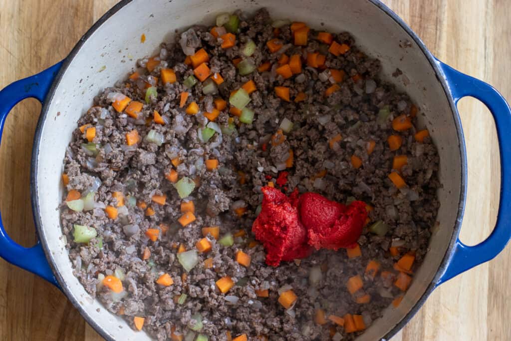 Tomato paste is added to sauteed beef and onions. beef.