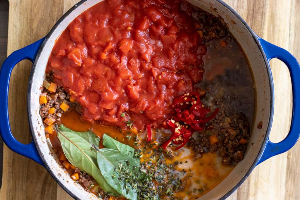 Tinned tomatoes, bay leaves, stock, milk and seasoning are added to the pan.