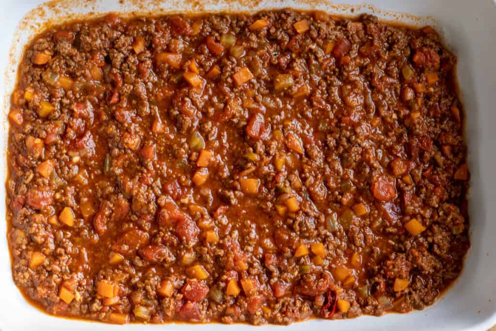 Meat sauce is spread to the bottom of a baking dish.