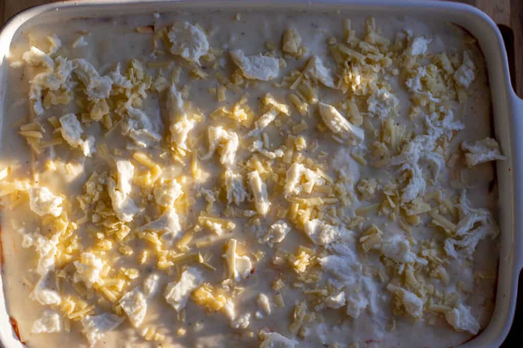 Layered lasagna is topped with cheese before baking.