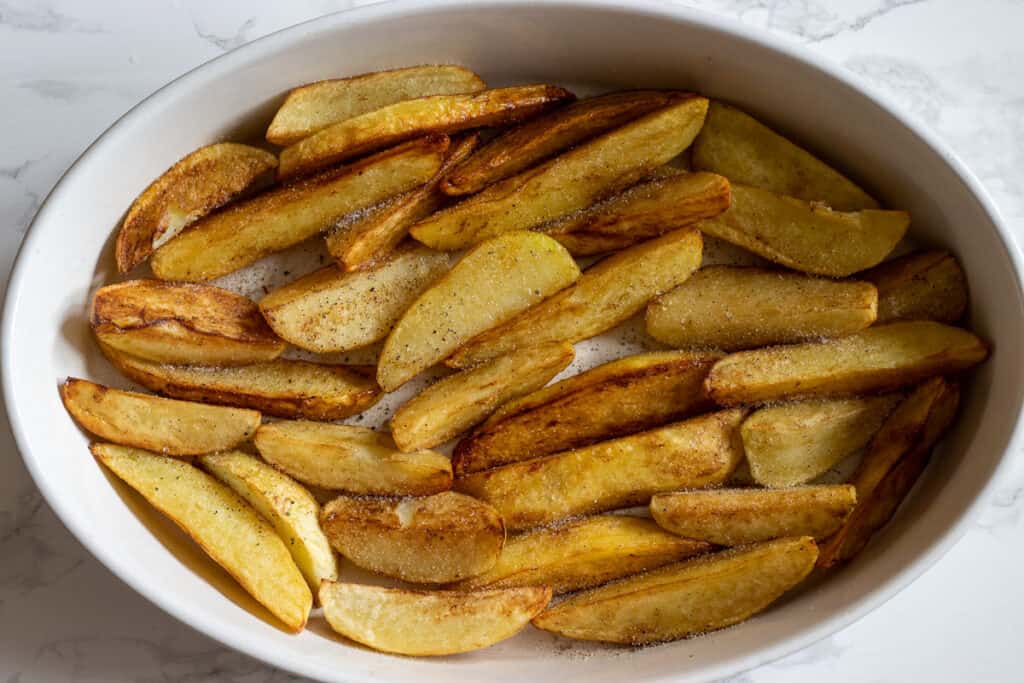 Lightly fried potatoes are layered on a baking dish/