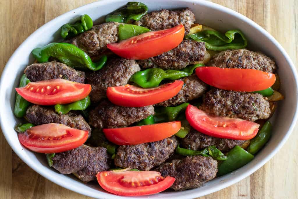 Meatballs, peppers and tomato wedges are scattered on top of potatoes.
