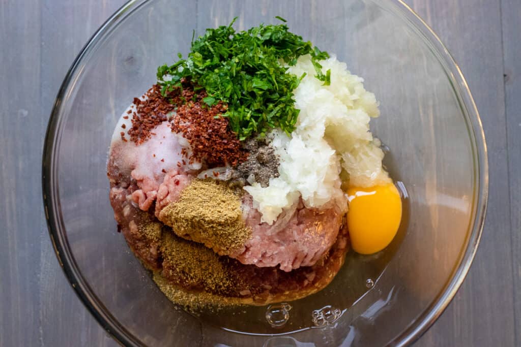 Ground beef, egg, parsley, onion, and spices are placed in a bowl.