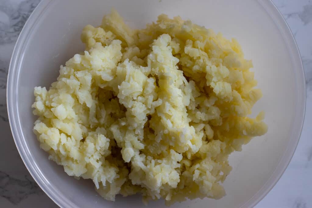 Boiled potatoes grated into a bowl.