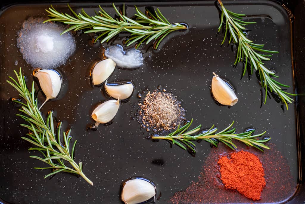 Garlic, rosemary, seasoning and duck fat in a baking tray.