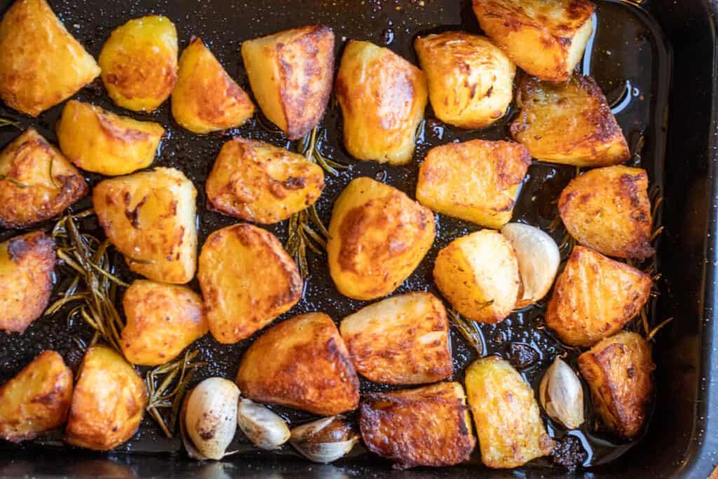Roasted potatoes turning golden and crisp in the tray.