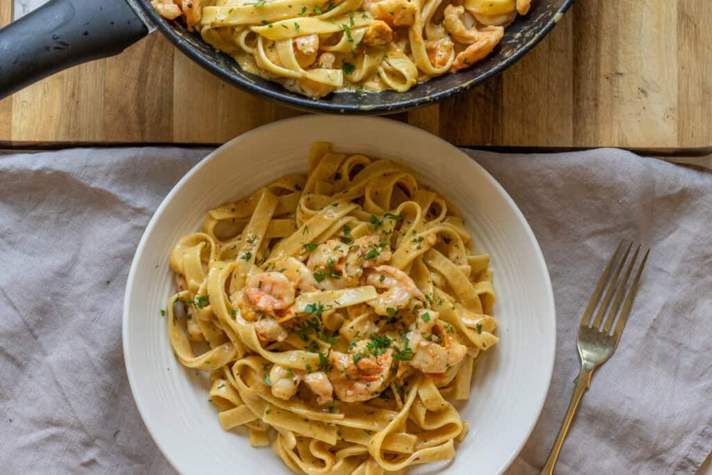 A serving bowl of the creamy shrimp pasta topped with parsley.