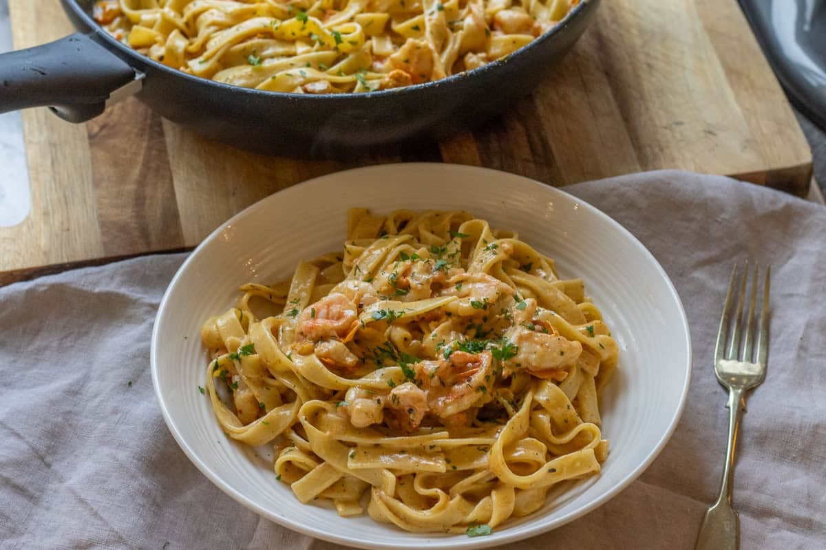 Cajun shrimp alfredo pasta served in a white bowl with the pan behind.
