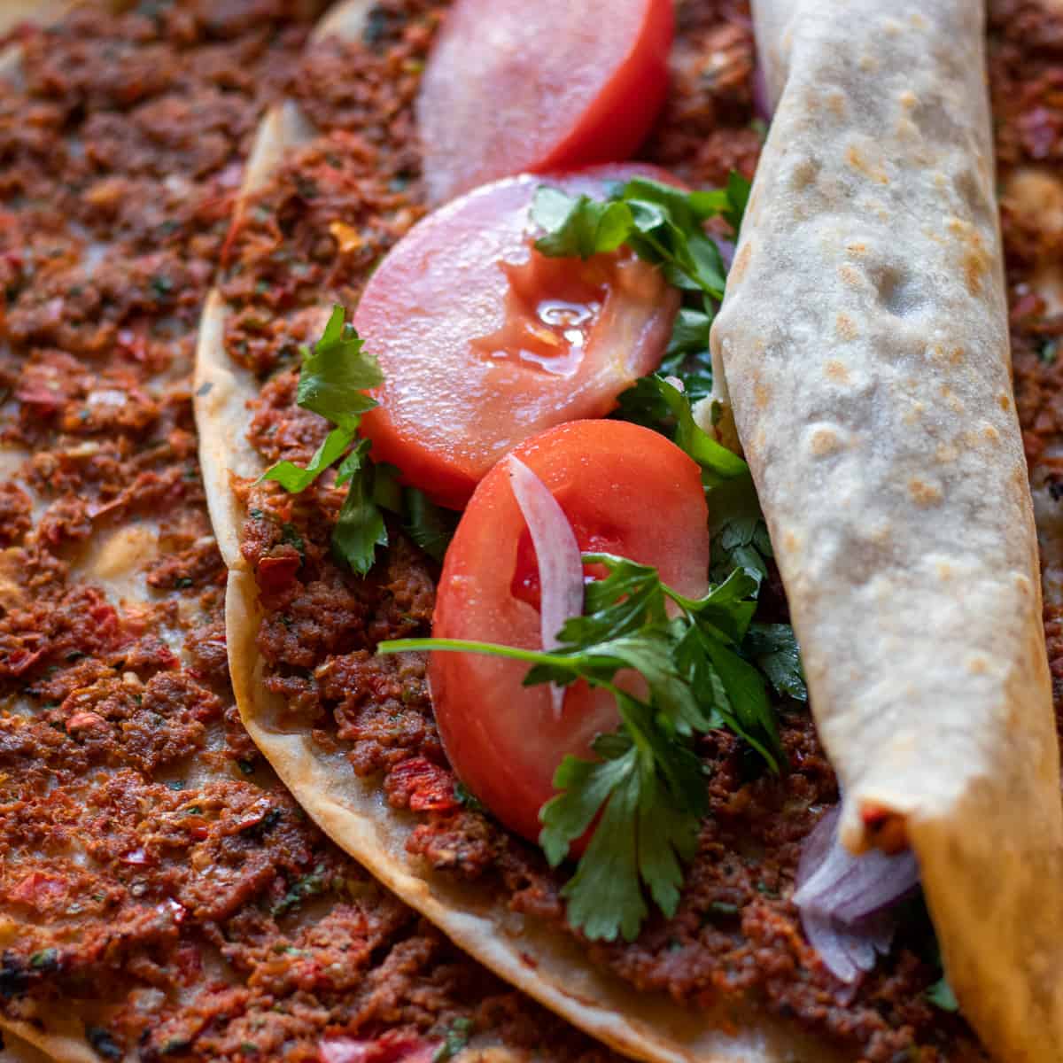 Turkish lahmacun served folded with sliced tomatoes and parsley