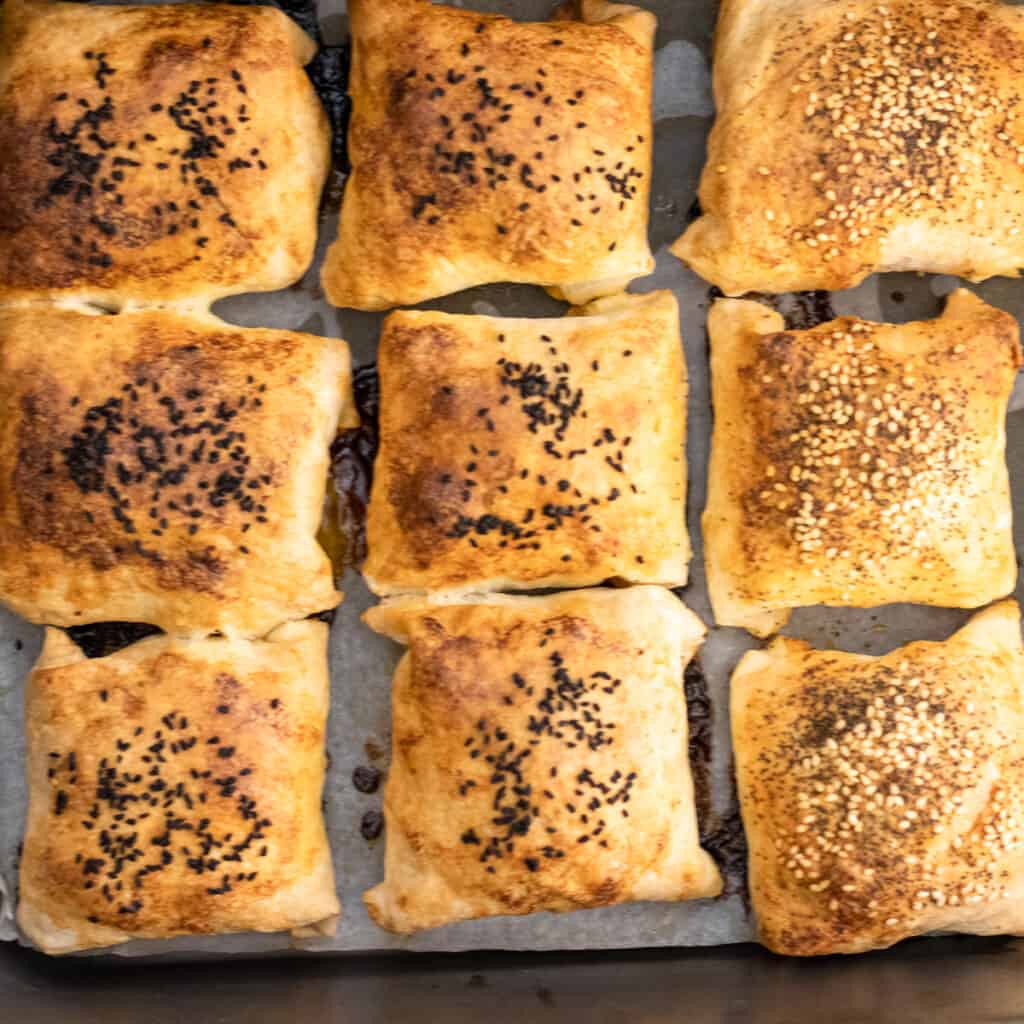 Baked kiymali borek parcels on a lined tray, some with nigella seeds and some with sesame.