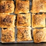 Baked kiymali borek parcels on a lined tray, some with nigella seeds and some with sesame.