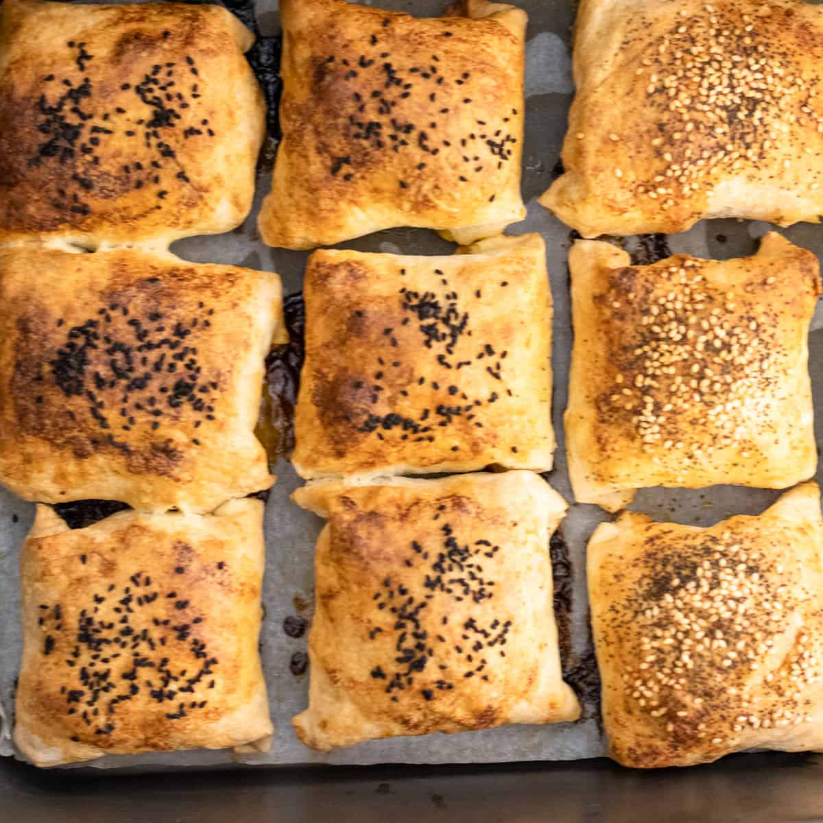 Baked kiymali borek parcels on a lined tray, some with nigella seeds and some with sesame.