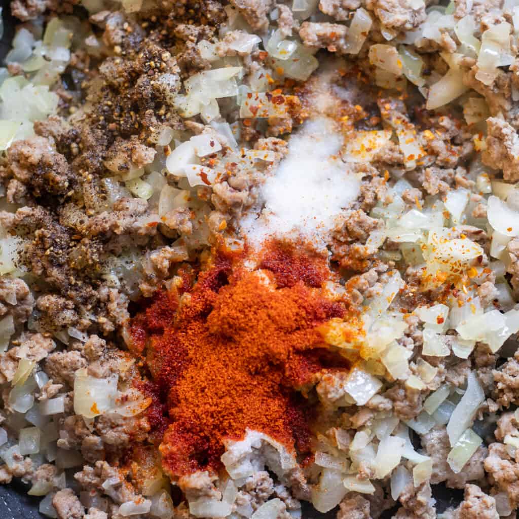 Salt, black pepper and paprika added to the meat and onions in the pan.