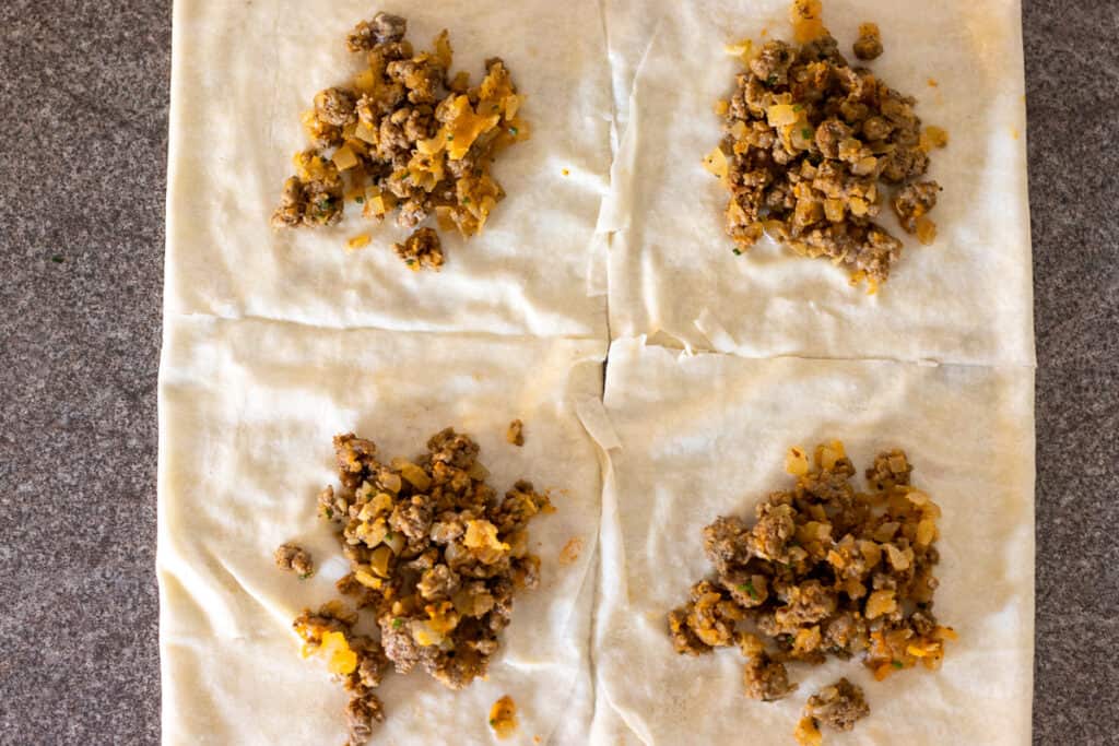 A spoonful of meat filling placed on each of the four yufka squares.