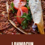 A rolled lahmacun with tomato and parsley, resting on a stack of Turkish flatbreads.