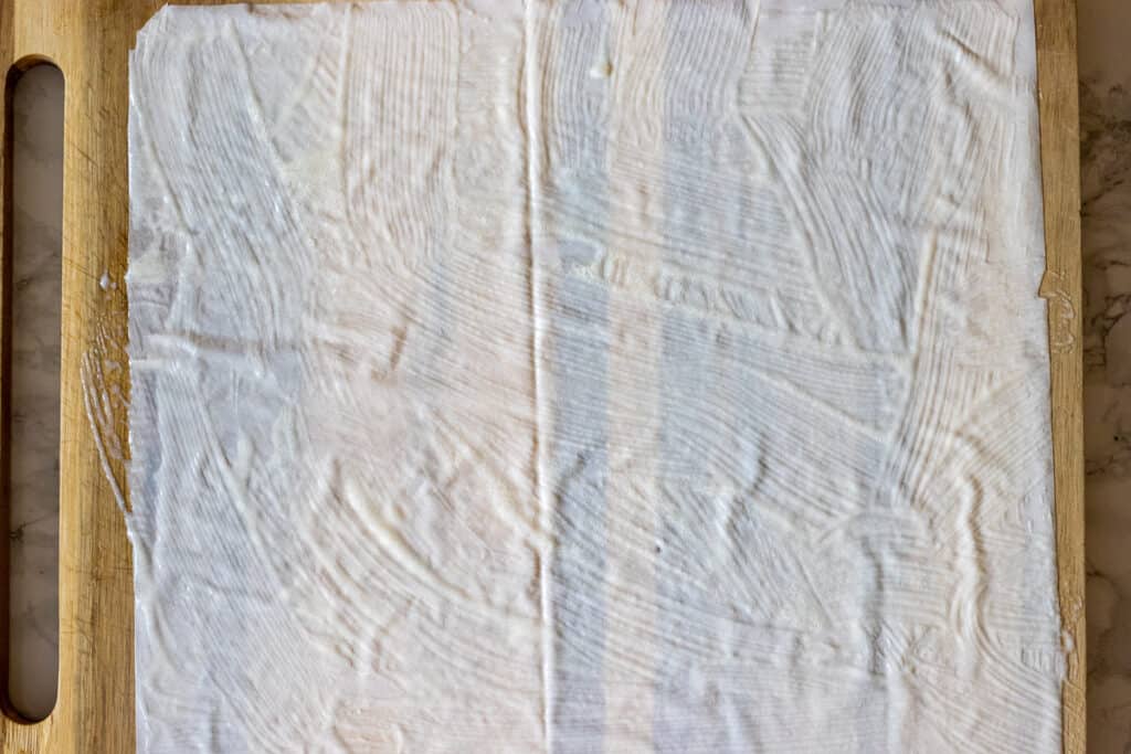 A sheet of filo is brushed with a milk and oil mixture.