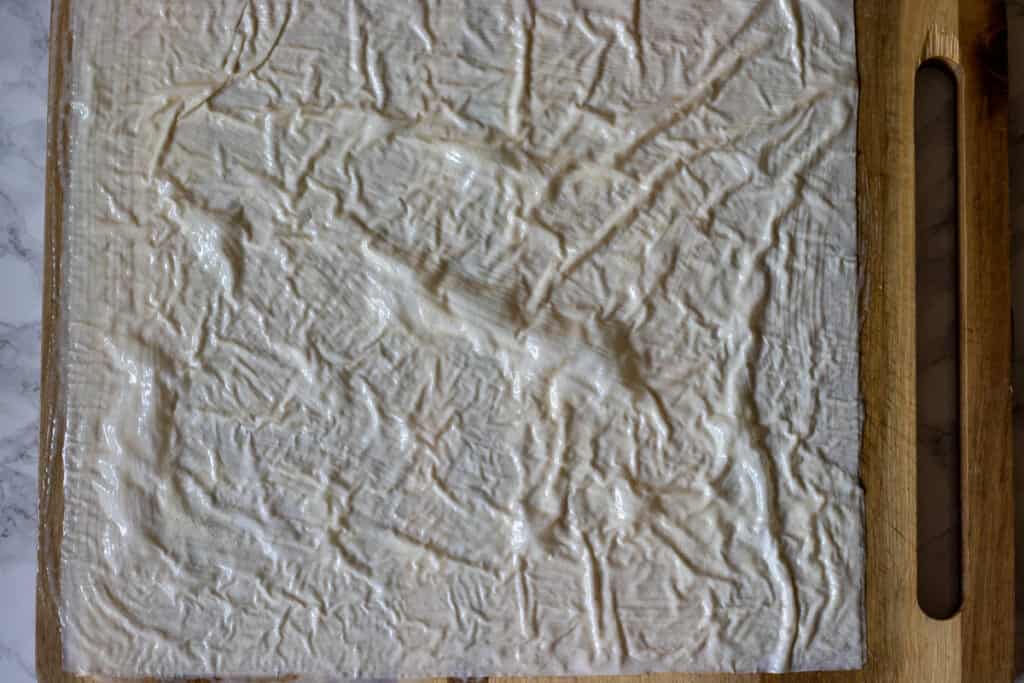 3 filo sheets are layered and brushed with sauce on a wooden board.