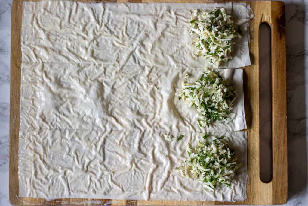 Phyllo pastry cut into strips with cheese filling spooned onto one end of each.