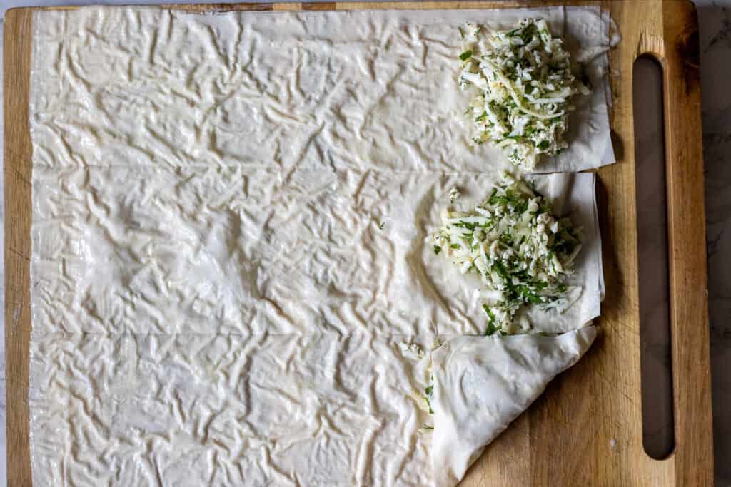 Phyllo strips with cheese filling being folded diagonally into triangles.