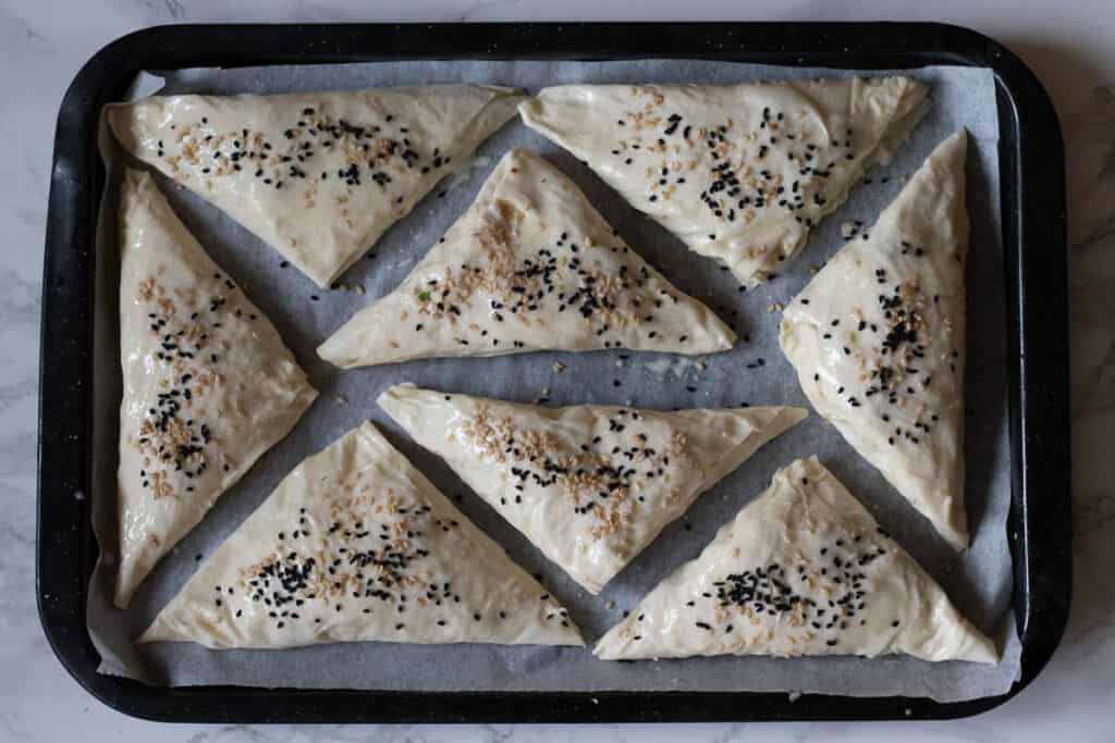 Unbaked cheese borek triangles brushed with egg wash and sprinkled with sesame and nigella seeds.
