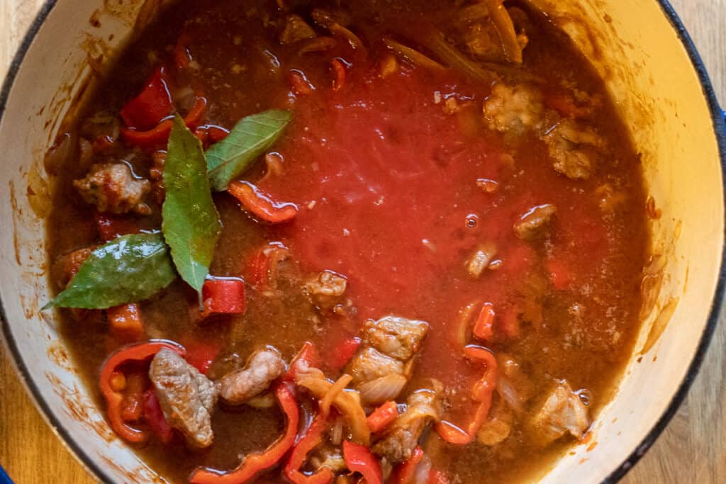 Chopped tomatoes, stock, and bay leaves added to the pan.