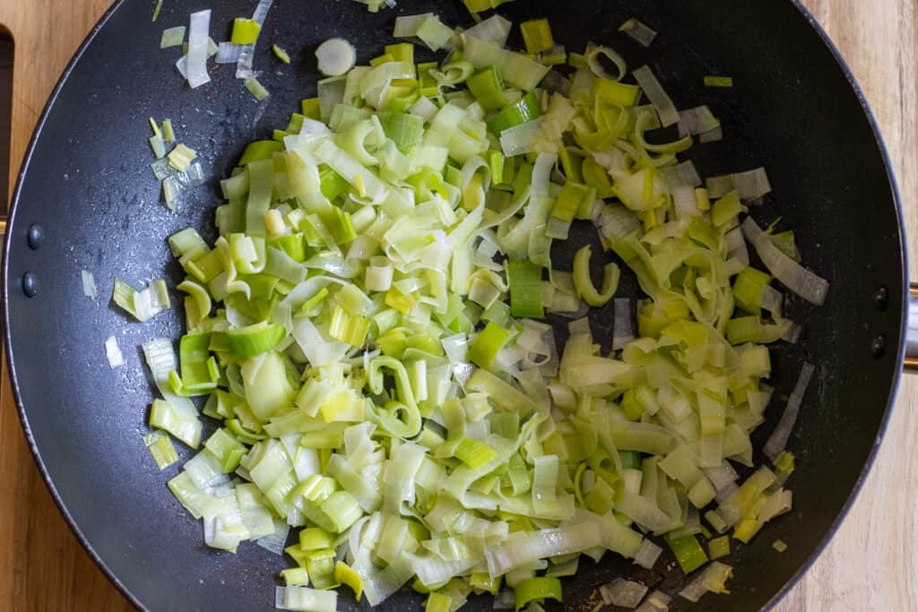 Sliced leeks softening in butter in a large pan.