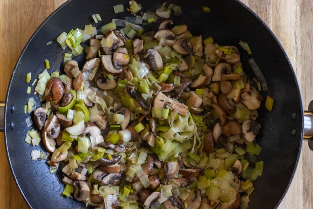 Sliced mushrooms added to the leeks in the pan.