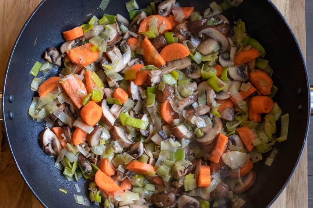 Sliced carrots added to the mushrooms and leeks in the pan.
