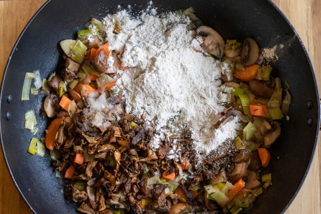 Flour, chopped porcini and black pepper added to the vegetables in the pan.