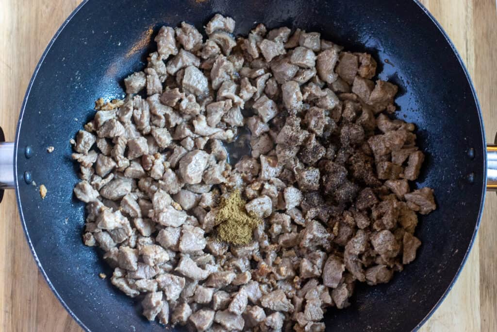 The spices are added to the sautéed lamb.