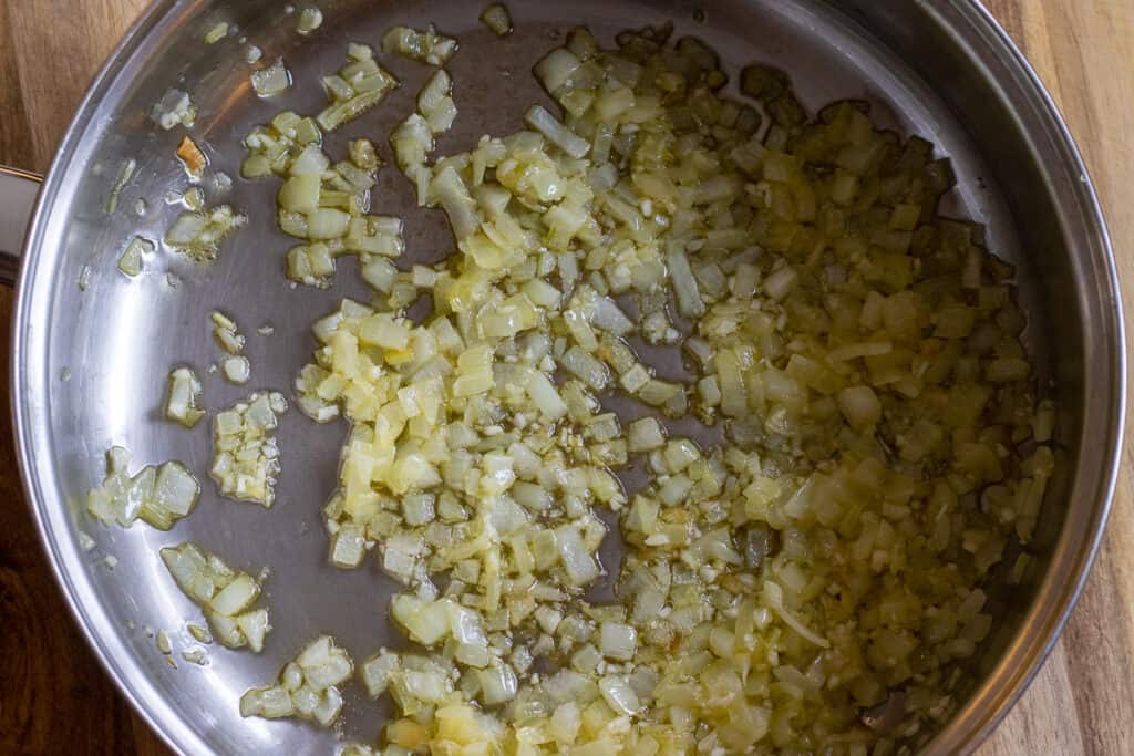 Chopped onions sauteing in ghee in a stainless steel pan.
